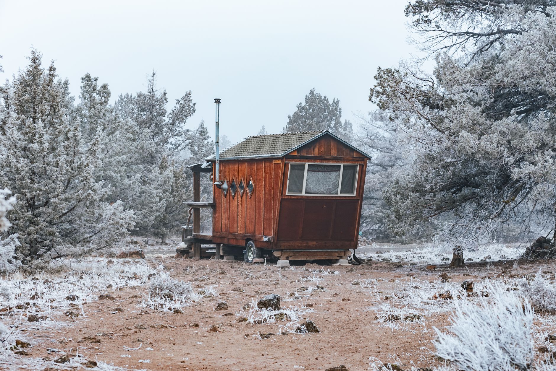 Small wooden cabin exterior with a loft window and compact kitchen visible through the doorway